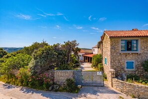 A stone house with a red-tiled roof, a gated entrance, and a view of the surrounding landscape.