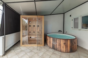 Ein Wellnessbereich mit einer Holzwanne, einer von Glas umschlossenen Sauna und einem gefliesten Boden.