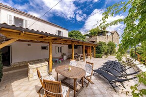 A covered outdoor patio with a table and chairs, a stone bench, and a stone wall.