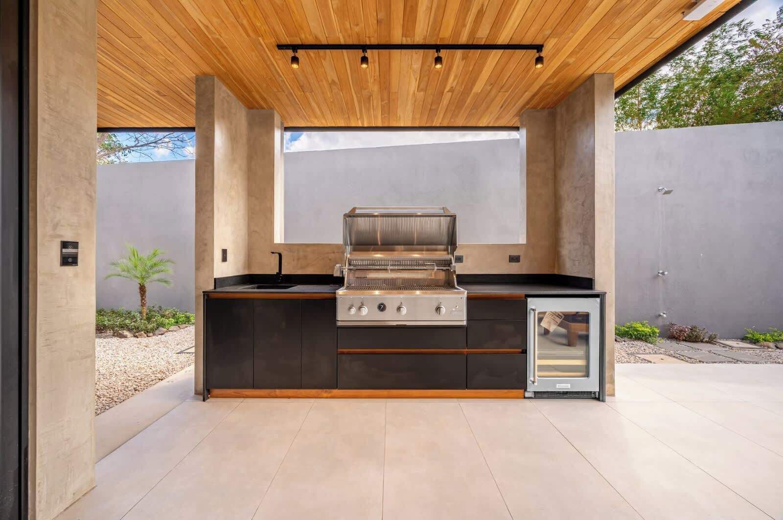Una cuina exterior moderna amb una barbacoa integrada, un refrigerador petit i un sostre de fusta.