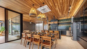 A modern kitchen with wooden ceiling, large windows, and a dining area with wooden chairs and tables. - Architect-Designed Villa Pool & Chef's Kitchen (Playa Grande)