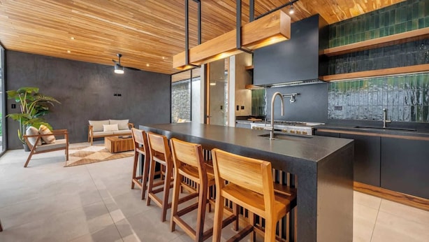 A modern kitchen with a central island, bar stools, and a dining area with a sofa and chairs. - Architect-Designed Villa Pool & Chef's Kitchen (Playa Grande)