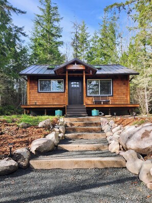 A wooden cabin with a dark front door, two windows on the side, and a porch with a bench. - Private Evergreen Hideaway (Sequim)