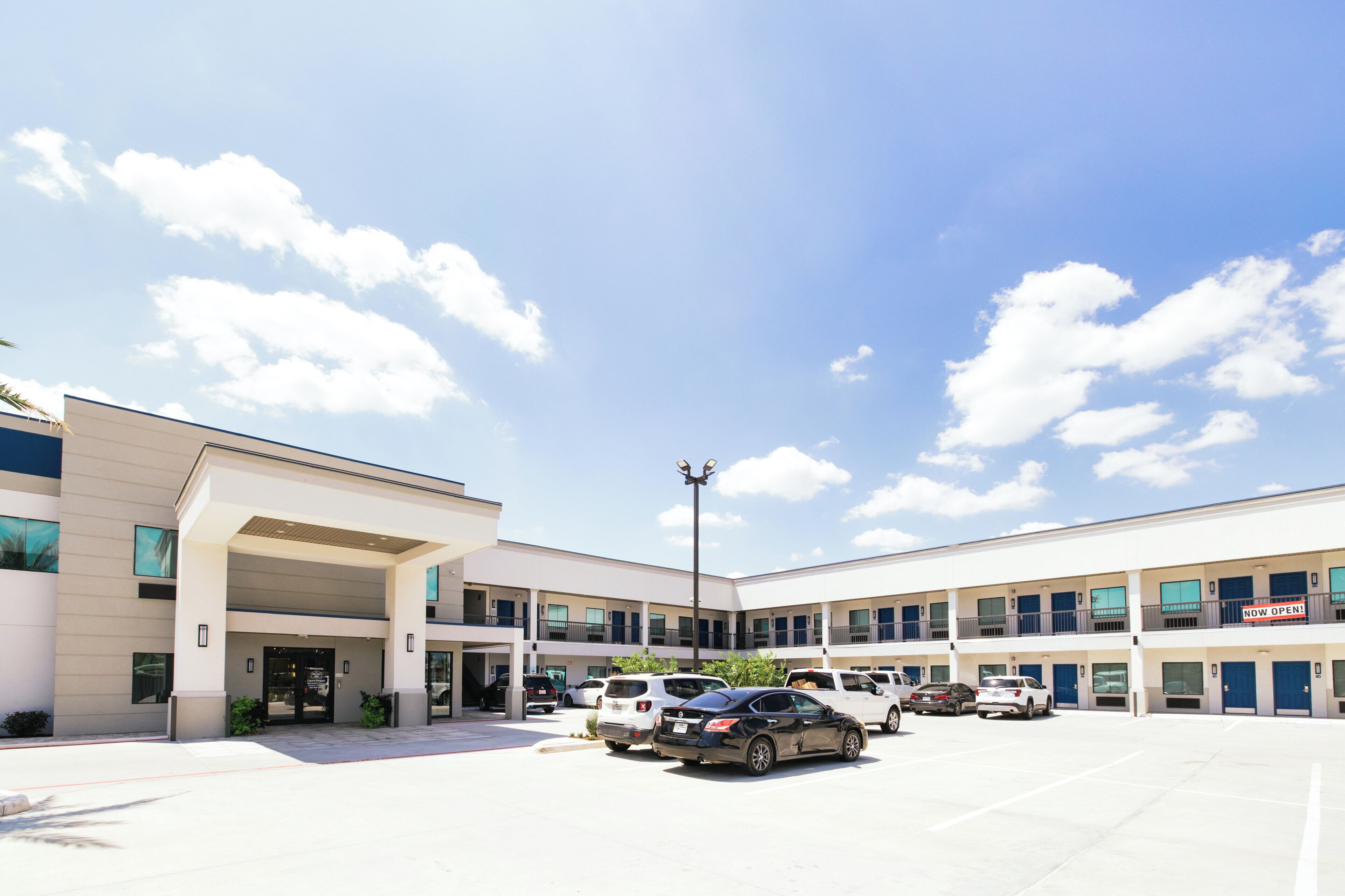 A multi-story hotel with a parking lot, a covered entrance, and a 'NOW OPEN' sign.