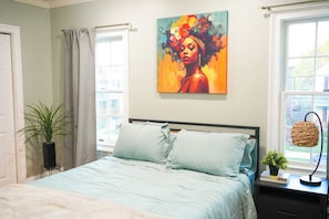 Een slaapkamer met een bed, een schilderij, een kamerplant en een raam.