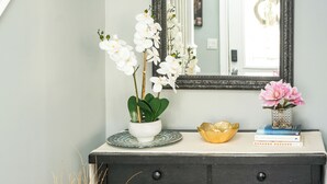 A dark wooden dresser with a mirror above it, a white vase with white flowers, a gold bowl, and a few books.