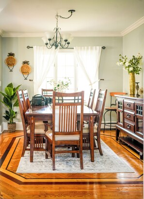 Een eetkamer met een houten tafel, stoelen, een kroonluchter en een kast.