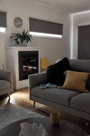 A living room with a grey sofa, a small table with a cup, a fireplace, and a plant.