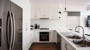 A modern kitchen with white cabinets, stainless steel appliances, and a wooden floor.