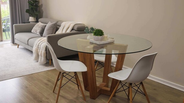 A modern living room with a glass-top dining table, white chairs, a grey sofa, and a potted plant. - Templestowe Village - 2BR, Parking, Pet-Friendly (Templestowe)