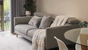 A grey sofa with a white throw blanket, a small table, and a potted plant. - Templestowe Village - 2BR, Parking, Pet-Friendly (Templestowe)
