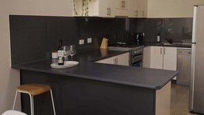 A modern kitchen with a black countertop, white cabinets, a stainless steel refrigerator, and a small island with a stool. - Templestowe Village - 2BR, Parking, Pet-Friendly (Templestowe)