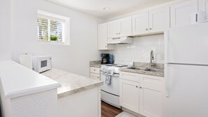 A modern kitchen with white cabinetry, a microwave, a stove, and a sink. - Bonfire Studio • King Bed • Pet Friendl (Lakeland)