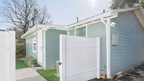 A small, single-story building with a white door, a small porch, and a green lawn. - Bonfire Studio • King Bed • Pet Friendl (Lakeland)