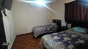 Quarto com duas camas, ventilador de teto, televisão e piso estampado.