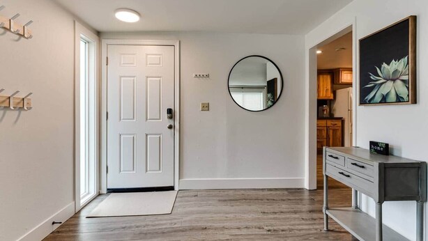 A hallway with a white door, a round mirror, a coat rack, and a small table with a 'home' sign. - TrackTown Retreat-Walk to Hayward Field & U of O (Eugene)