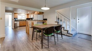 A spacious kitchen with wooden cabinets, a dining table with chairs, and a staircase leading to a second floor. - TrackTown Retreat-Walk to Hayward Field & U of O (Eugene)