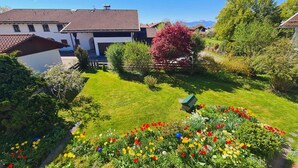 Ett bostadsområde med en välskött gräsmatta, ett stort utbud av blommande växter och ett hus med ett tak täckt av takpannor.