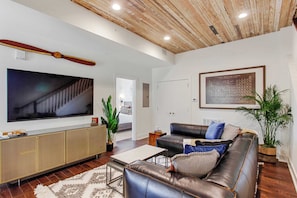 Un salon moderne doté d’un grand téléviseur à écran plat, d’un canapé en cuir, d’un plafond en bois et d’un tableau représentant le tableau périodique des éléments.