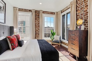 Une chambre à coucher avec un lit, une commode, une chaise et une fenêtre avec des rideaux.