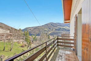 Un balcon offrant une vue sur un paysage montagneux, avec une balustrade en bois et un bâtiment doté d’un toit en pente.
