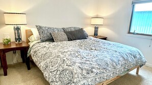 A bedroom with a bed, two bedside tables, two lamps, a window, and a carpeted floor.