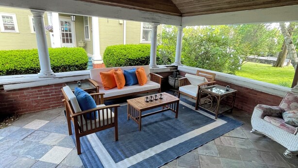 Un patio cubierto con piso de piedra, techo de madera y zona de estar con sofá y sillones.
