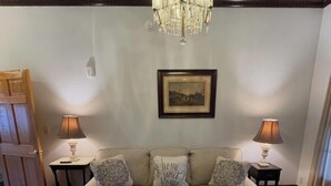 Una sala de estar con un sofá, dos mesitas auxiliares, una araña, un cuadro enmarcado y una alfombra estampada.