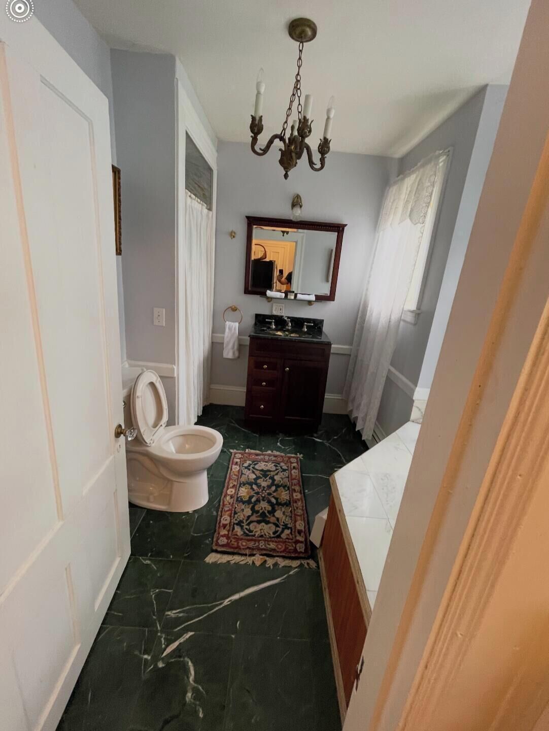A bathroom with a toilet, sink, mirror, and chandelier.