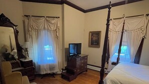 Un dormitorio con cama con dosel, ventilador de techo, televisor y una silla.