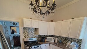 Una cocina con gabinetes blancos, una araña, una estufa, un microondas y piso de madera.
