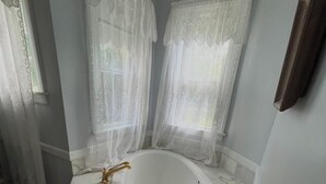 Un baño con una bañera independiente, encimera de mármol y una ventana con cortinas de gasa.