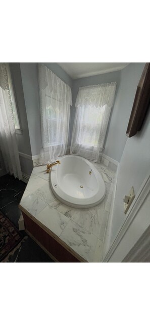 A bathroom with a freestanding bathtub, a marble countertop, and a window with sheer curtains.