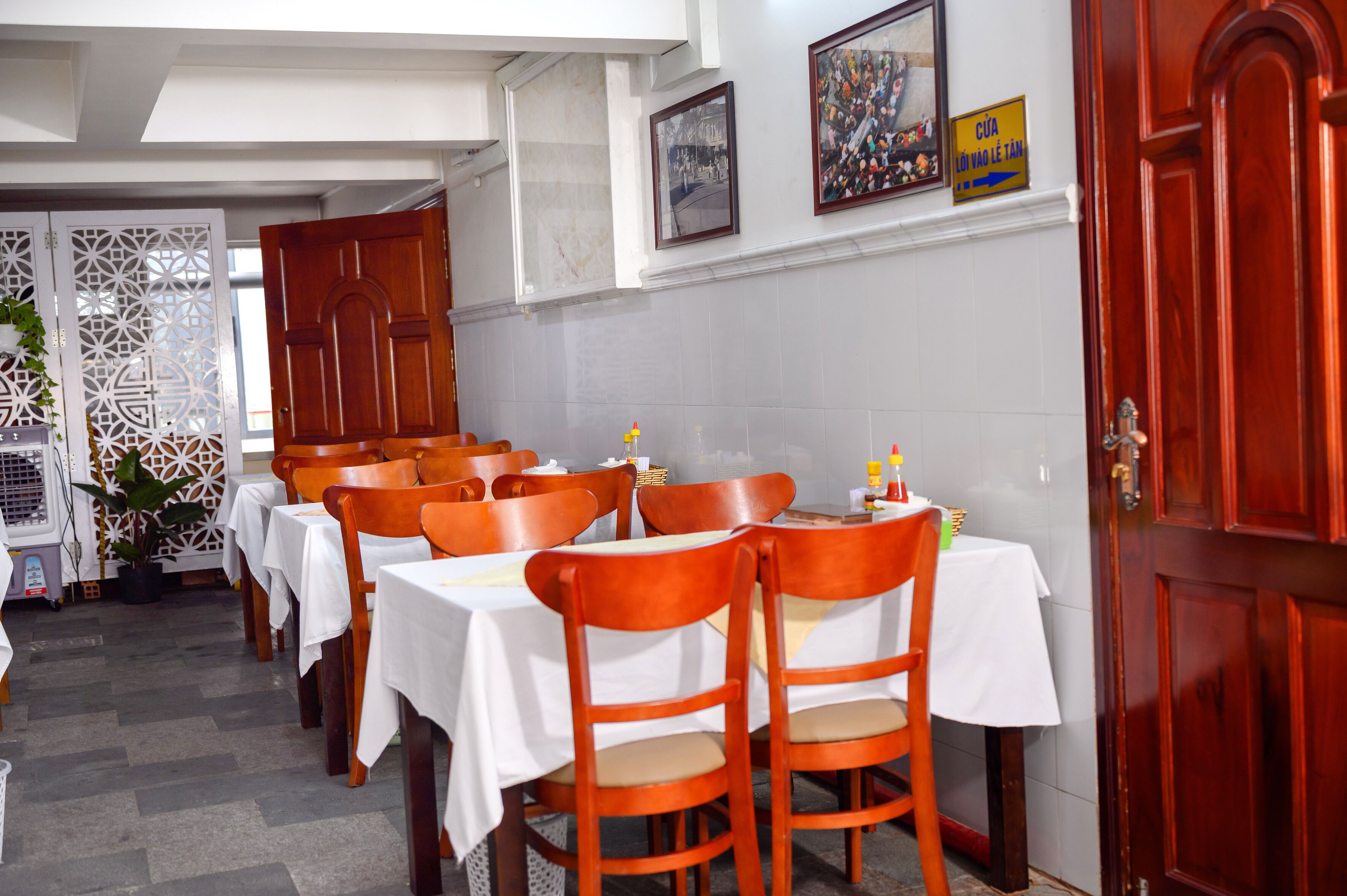 A restaurant interior with tables set for dining, wooden chairs, and a decorative wall.
