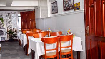 A restaurant interior with tables set for dining, wooden chairs, and a decorative wall.