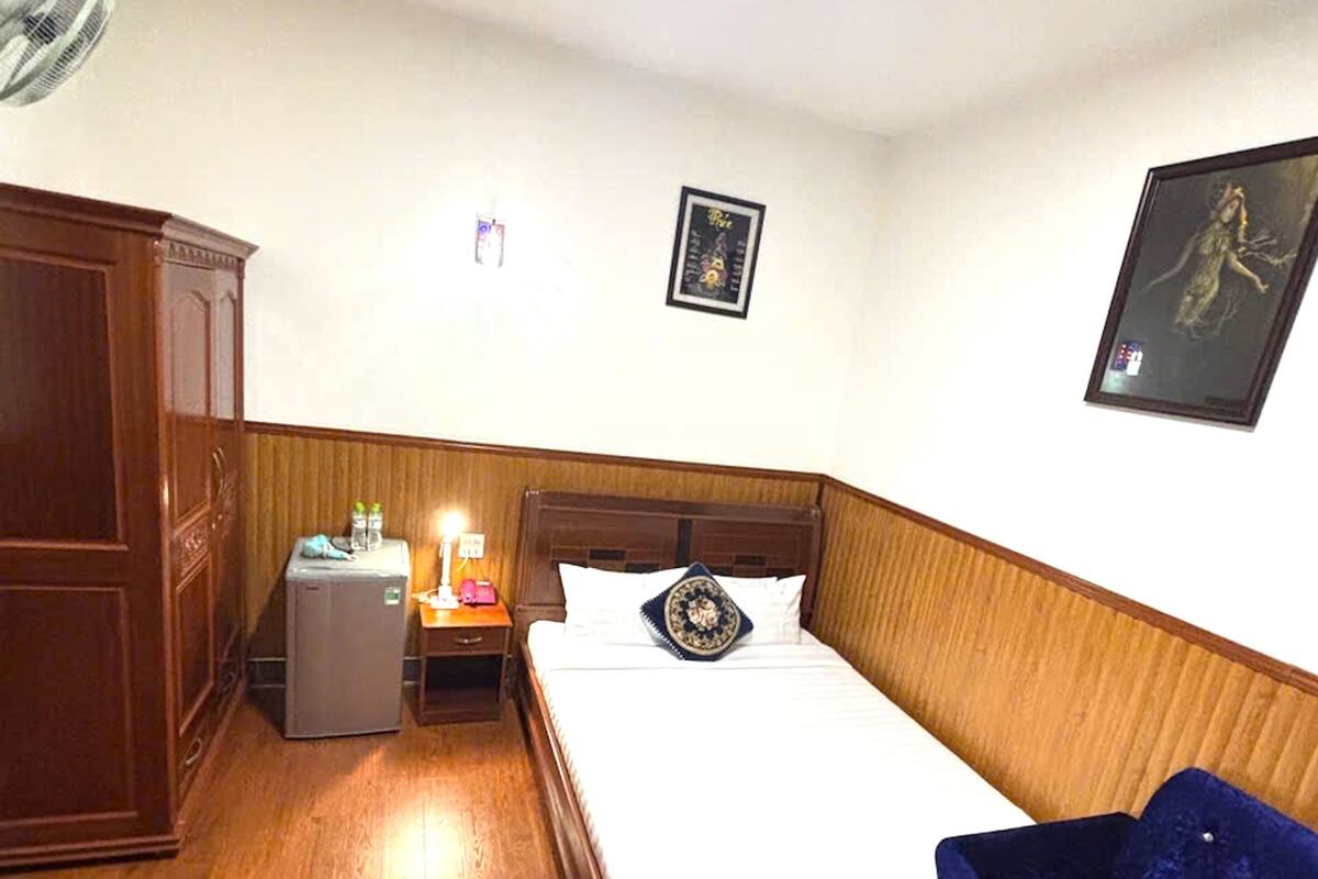 Une chambre à coucher comprenant un lit, une table de chevet, une commode, un radiateur et un tableau accroché au mur.