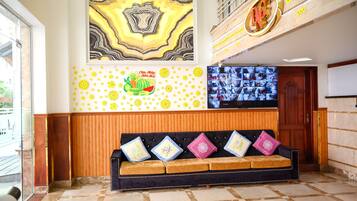 A reception area with a black sofa, a wall-mounted TV, and a large abstract painting.