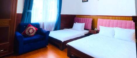 Habitación de hotel con dos camas, un armario de madera, un sofá azul y una ventana con cortinas.