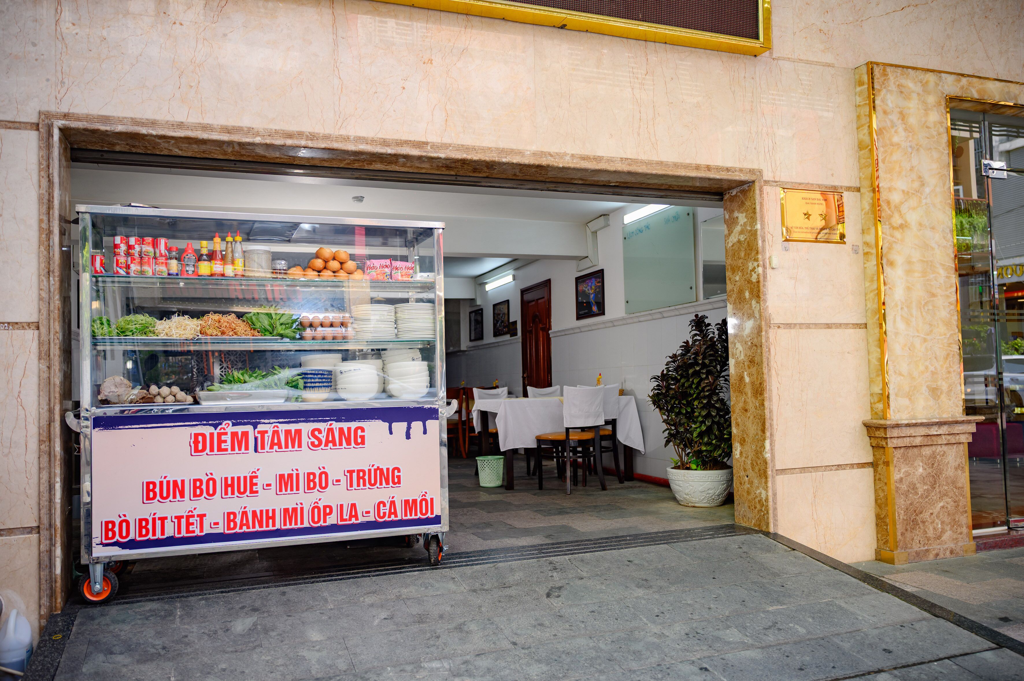 A food cart outside a building with a sign listing items like noodles, eggs, and vegetables.