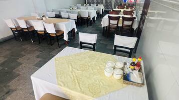 A restaurant with multiple tables and chairs, some covered with white tablecloths.