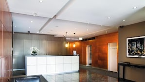A modern hotel lobby with a reception desk, a potted plant, and a cityscape artwork on the wall. - Exclusive Stays - The Sentinel  (Southbank)