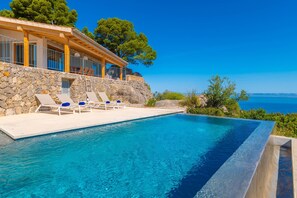 Une piscine à l’eau d’un bleu cristallin, des chaises longues et un mur en pierre.