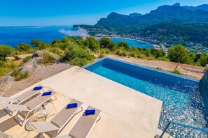 Una piscina con sillones de descanso y vistas a un pueblo costero y montañas.