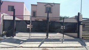 A gated entrance with a metal gate, a paved driveway, and a building with a pink facade and a white door. -  Casa Villegas B céntrica en Linares - WiFi 100MB y asador (Linares)