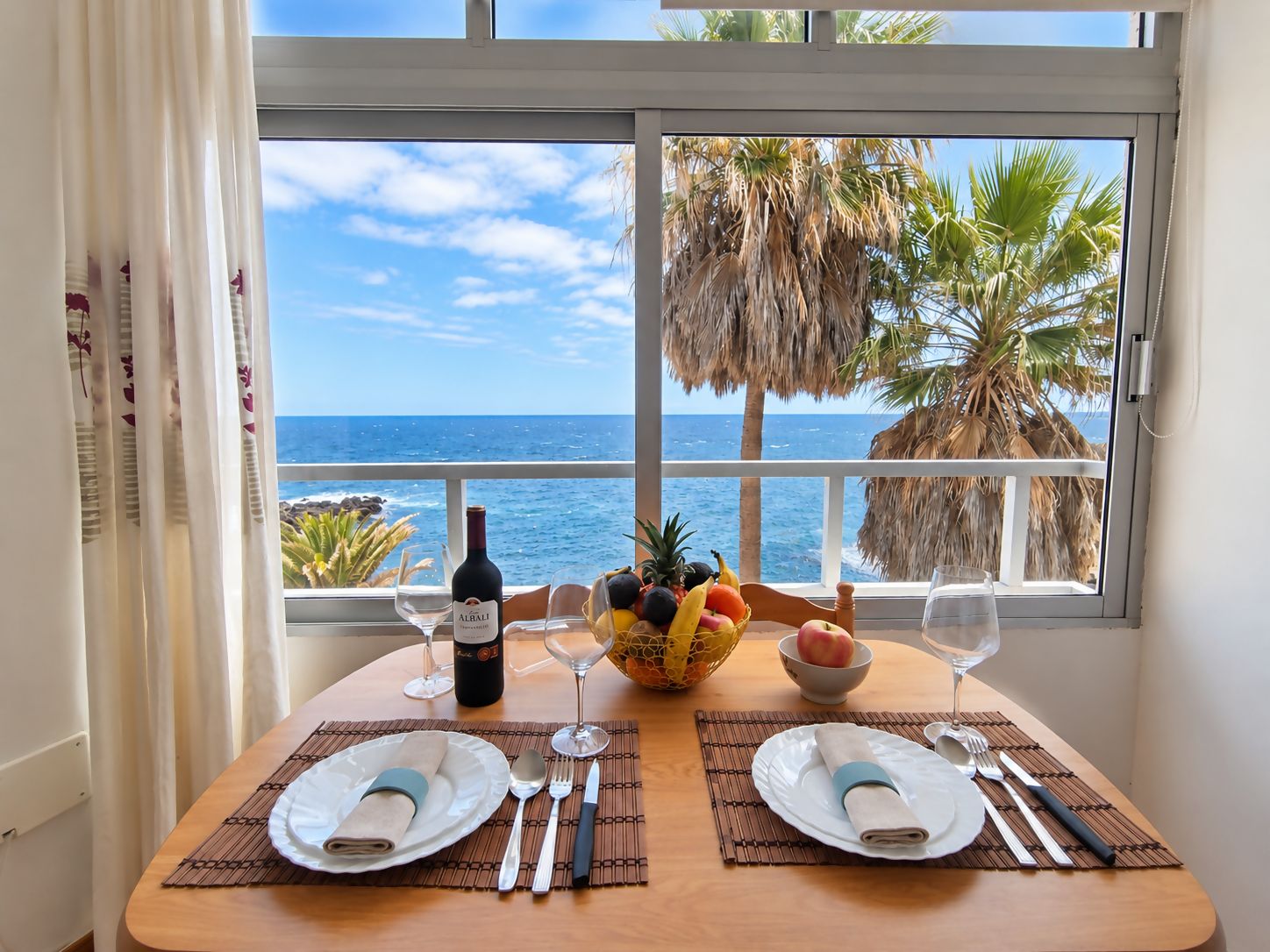 A dining table set for two with a view of the ocean and palm trees.