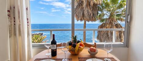 A dining table set for two with a view of the ocean and palm trees.