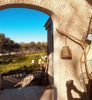 Ein rundbogiger Durchgang, der in einen Garten mit Blick auf ferne Berge führt, mit einem hängenden Korb und einer rustikalen Mauer.