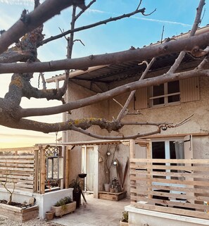 Ein rustikales Haus mit einer Holzpergola, einem kleinen Garten und einem Fenster.