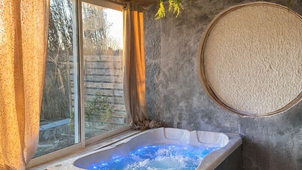 A hot tub in a wooden cabin with a stone wall and a large round mirror. - 2-bedrooms entire villa with jacuzzi and garden in charming Provence (S énas)