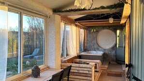 A room with a wooden table, chairs, a bench, a bathtub, and a view of the outdoors. - 2-bedrooms entire villa with jacuzzi and garden in charming Provence (Sénas)